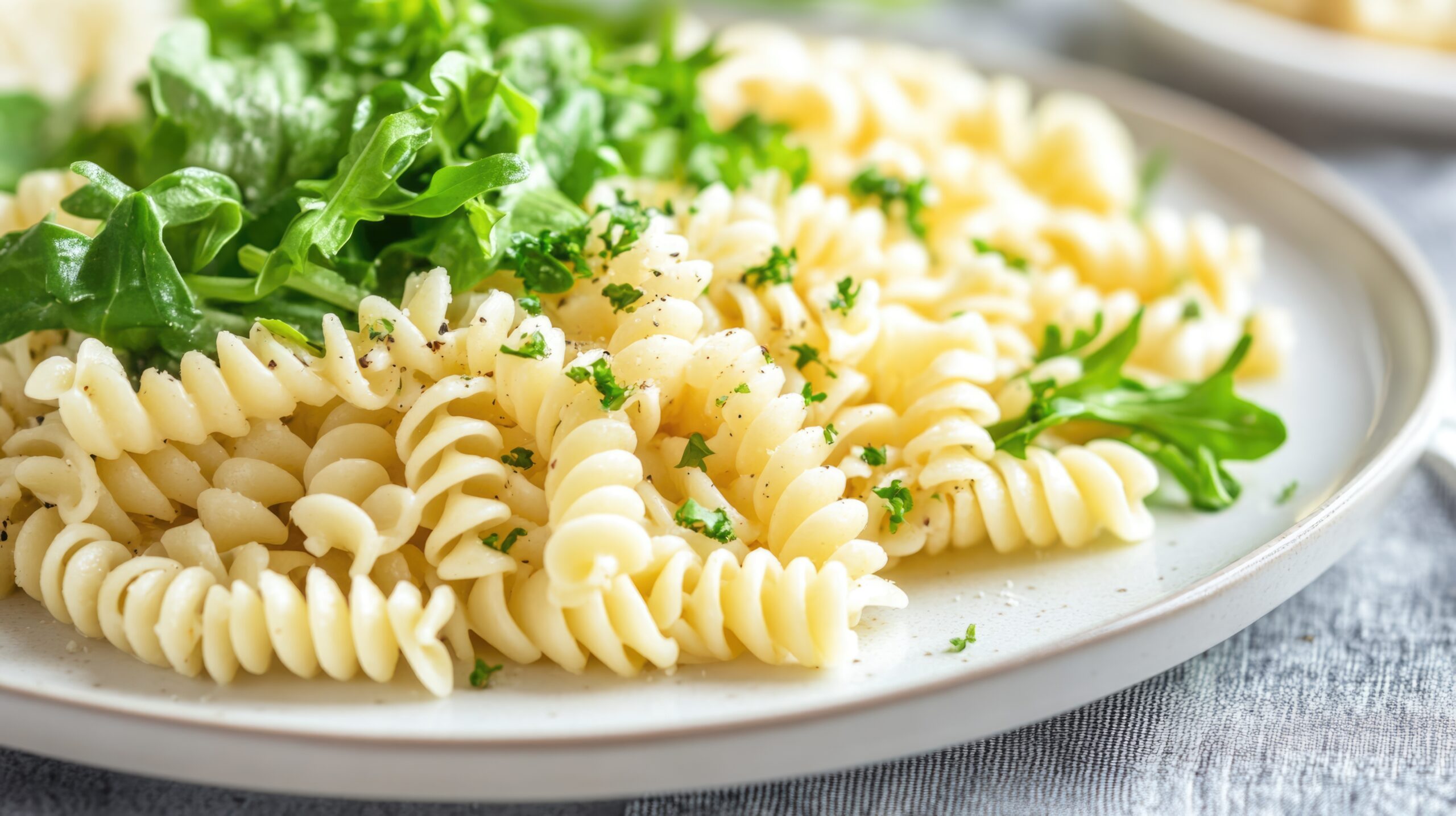Fusilli pasta served with fresh arugula garnished with herbs on a white plate with copy space