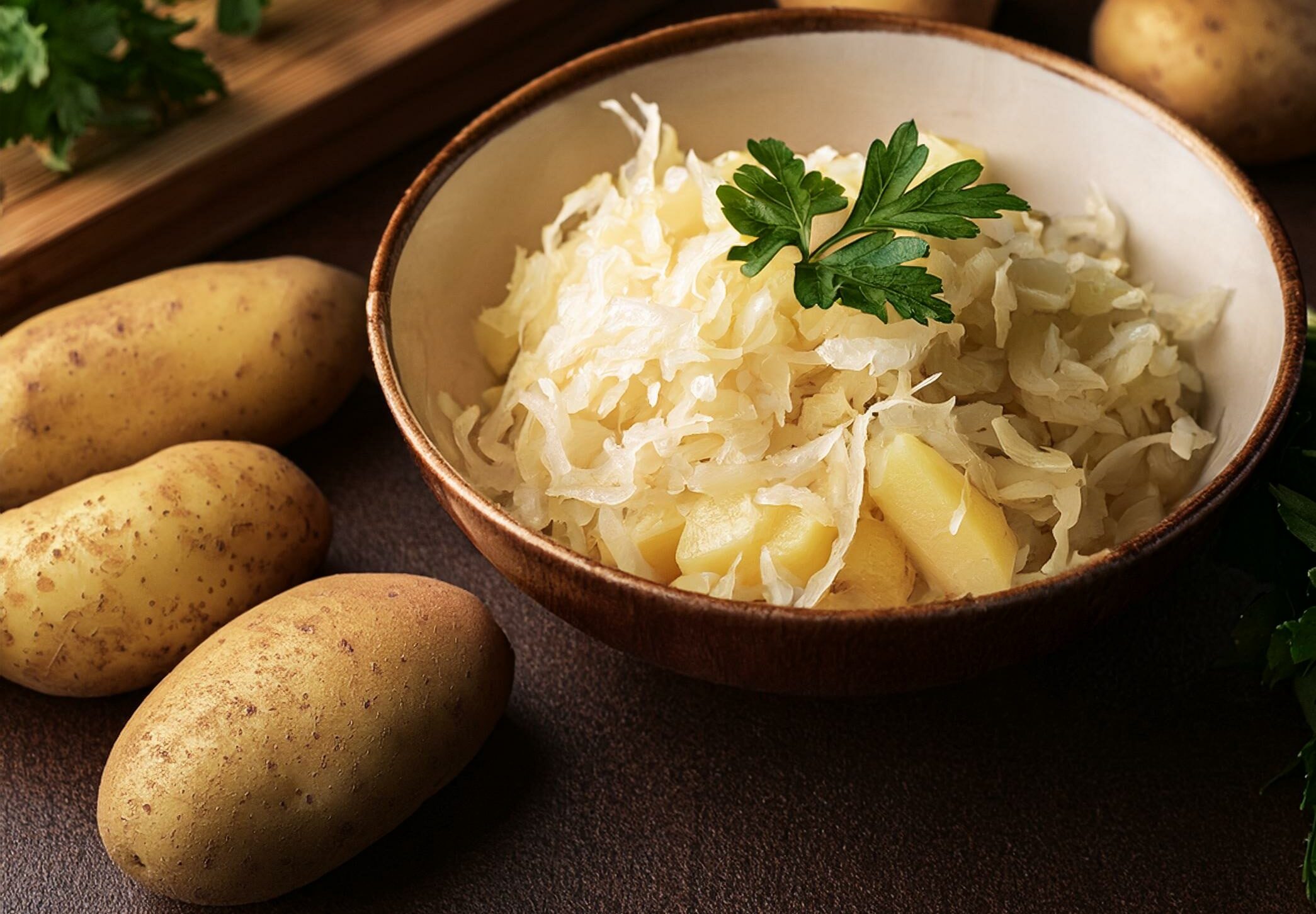 delicious homemade sauerkraut with potatoes garnished with parsley beside fresh potatoes