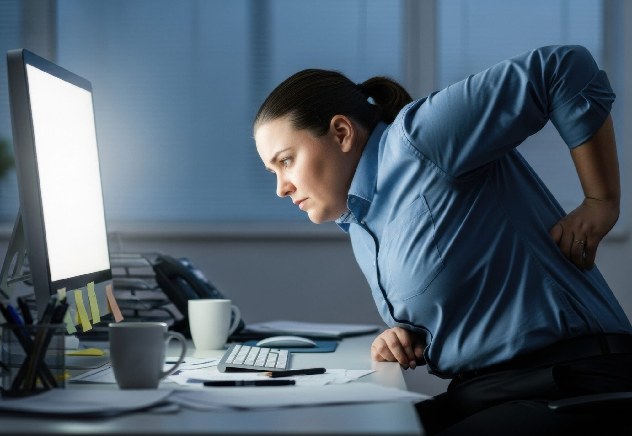Woman office worker with back pain from sitting at desk all day computer work ergonomics posture health problem