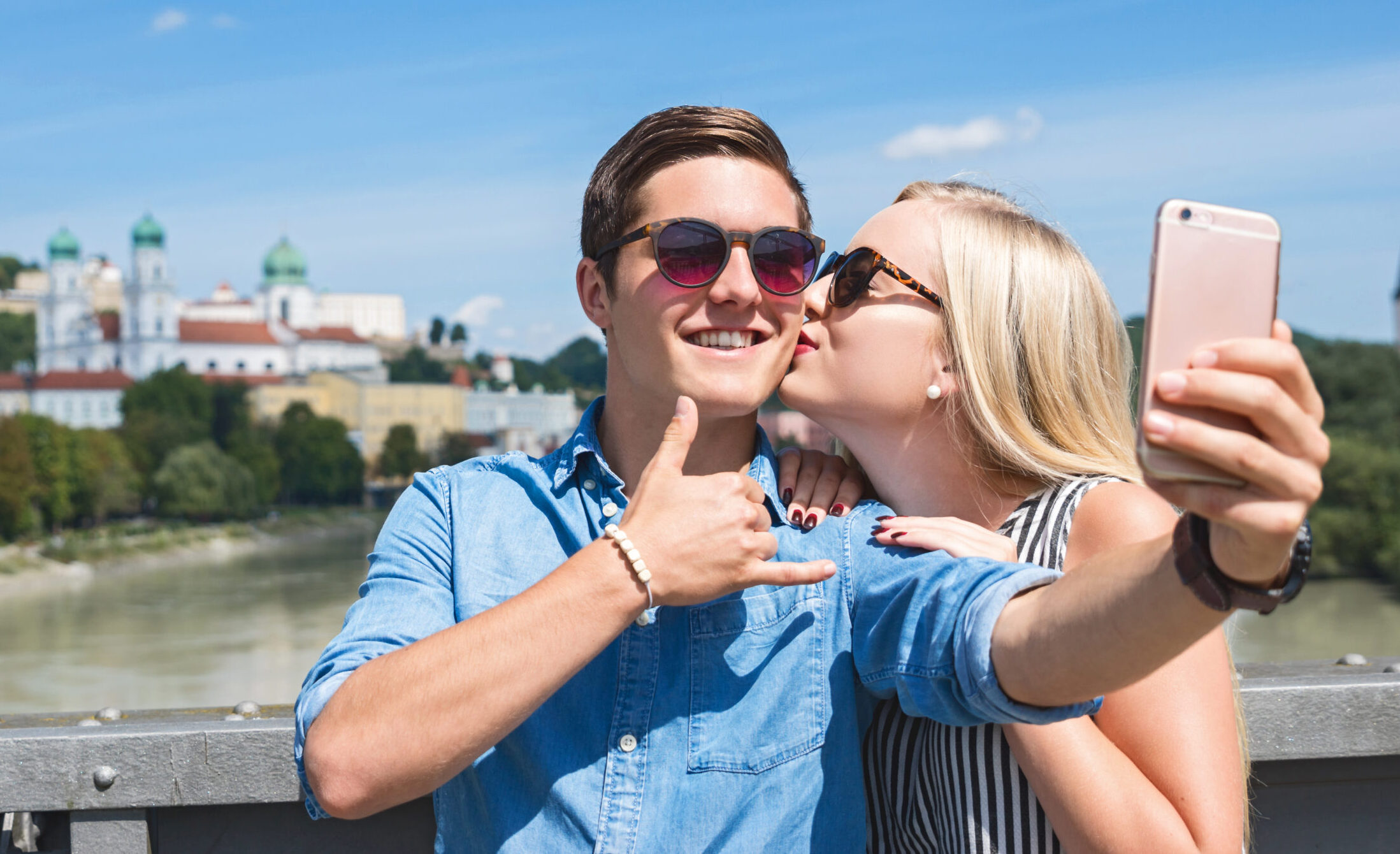 Frau küsst ihren Freund auf die Wange, während dieser einen Selfie macht