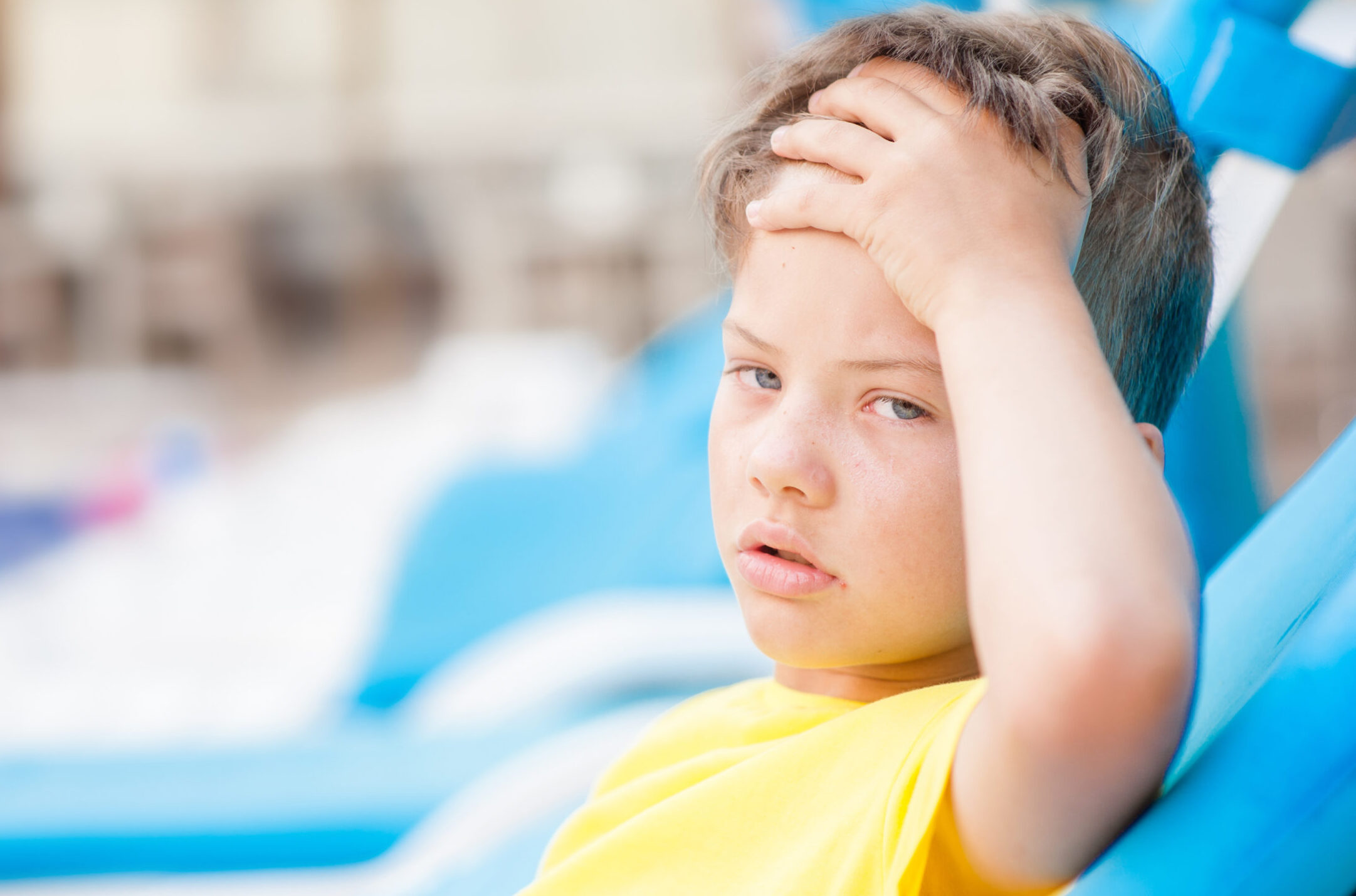 Little boy on the beach with a sunstroke touches his forehead, checking the temperature