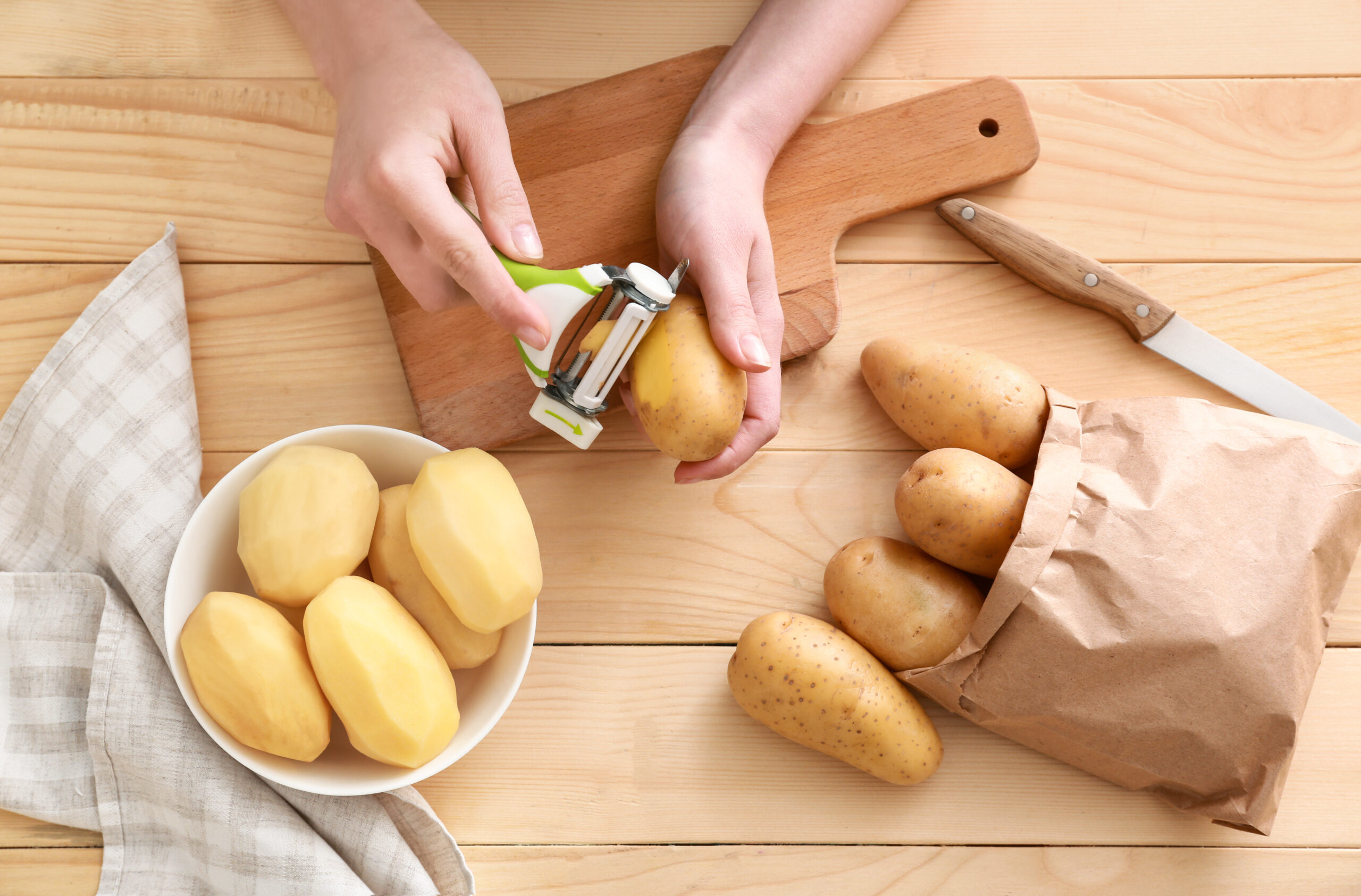 Woman peeling raw potato at wooden table
