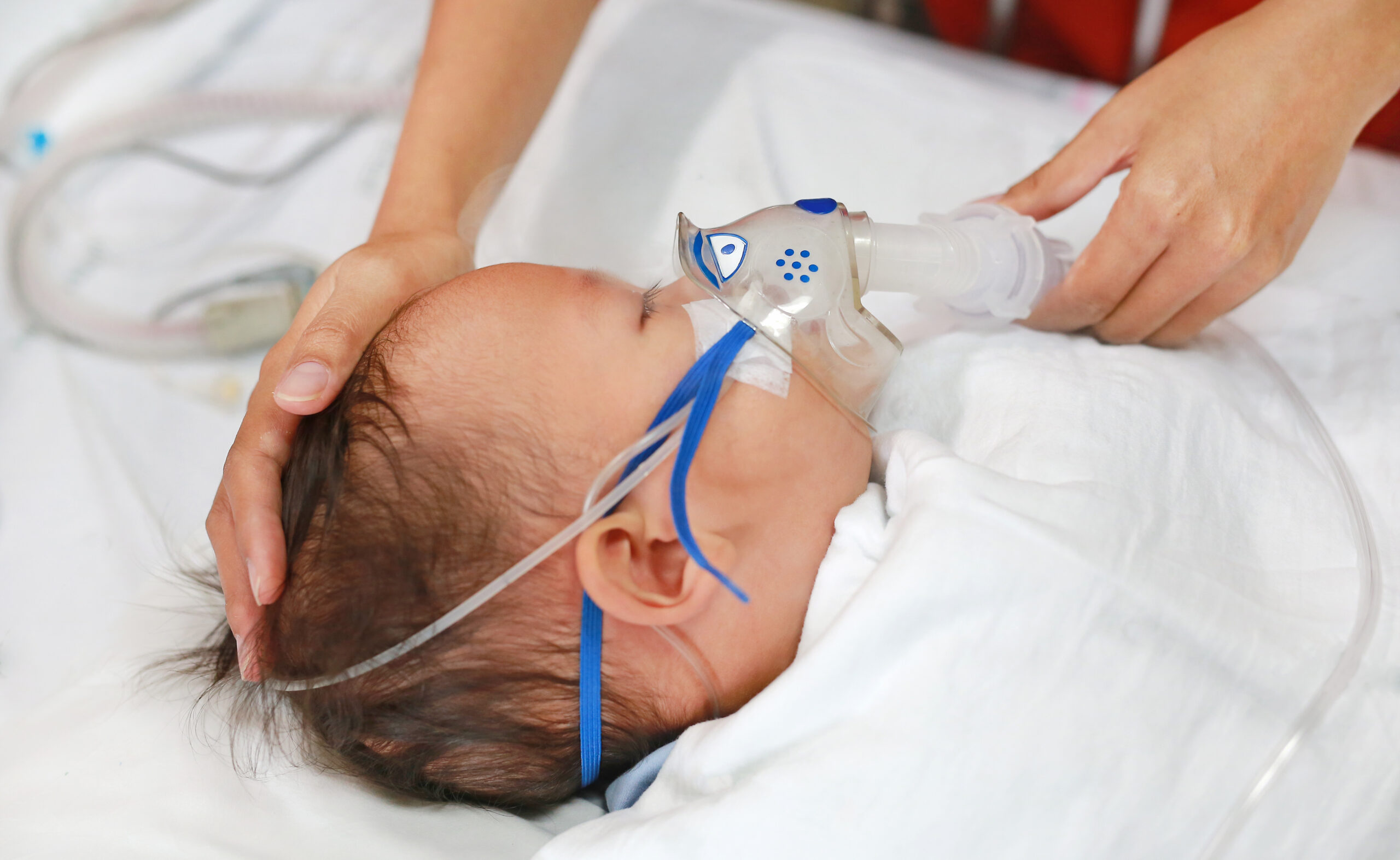 Toddler boy using nebulizer to cure asthma or pneumonia disease . Sick baby boy rest on patients bed and has inhalation therapy by the mask of inhaler. Respiratory Syncytial Virus (RSV).