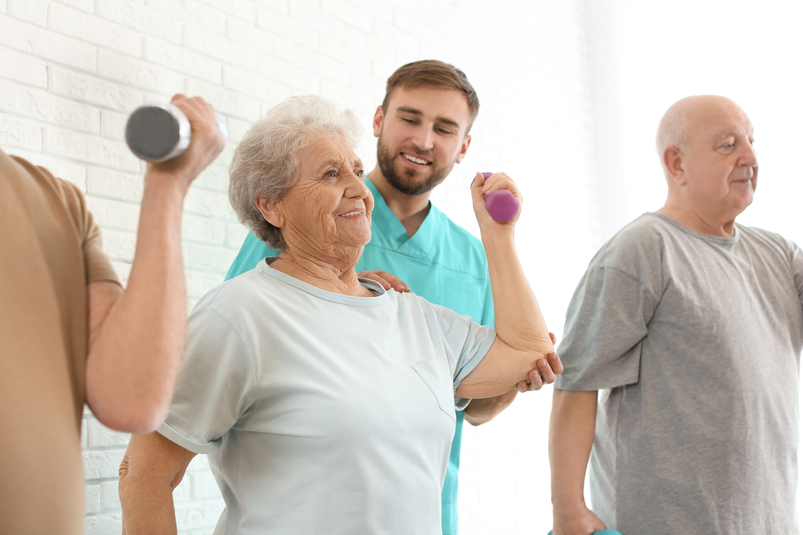 Care worker helping elderly woman to do exercise with dumbbell in hospital gym