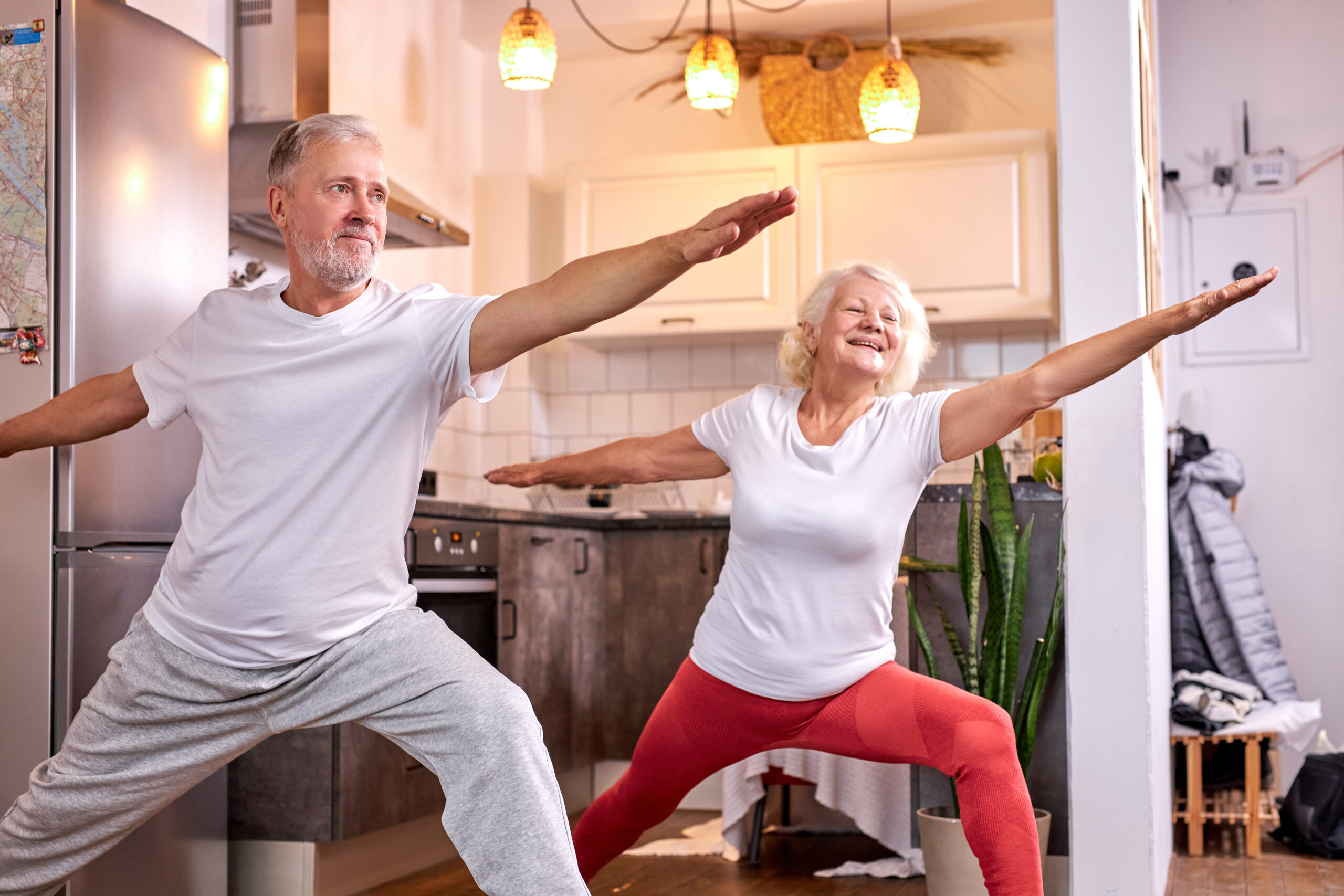 elderly man and woman practicing Virabhadrasana pose at home