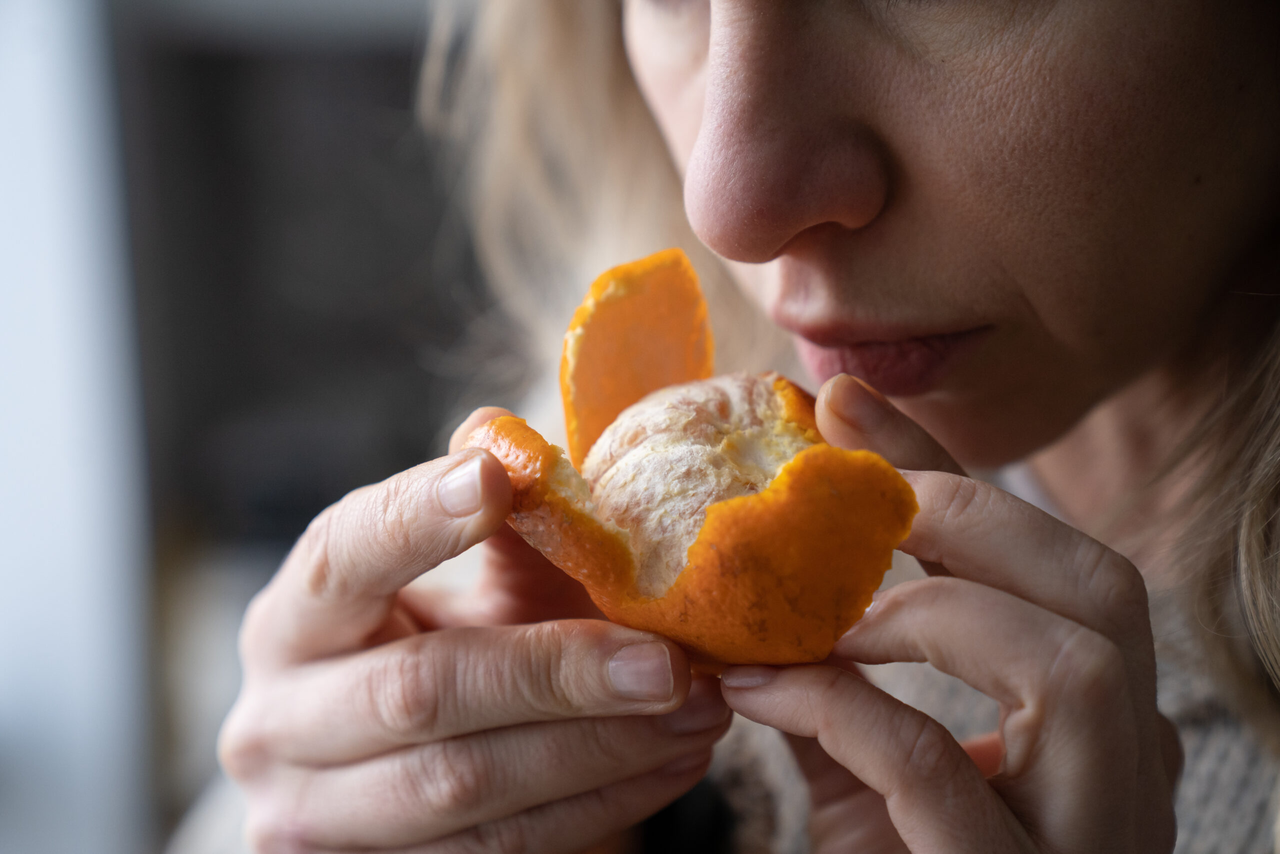 Sick woman trying to sense smell of fresh tangerine orange, has symptoms of Covid-19, corona virus