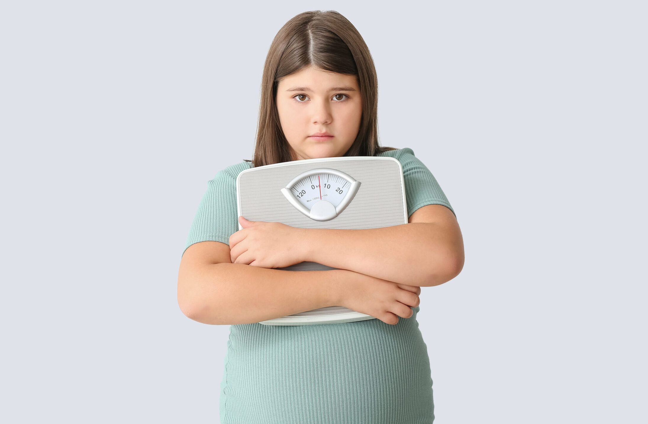 Sad overweight girl with measuring scales on light background