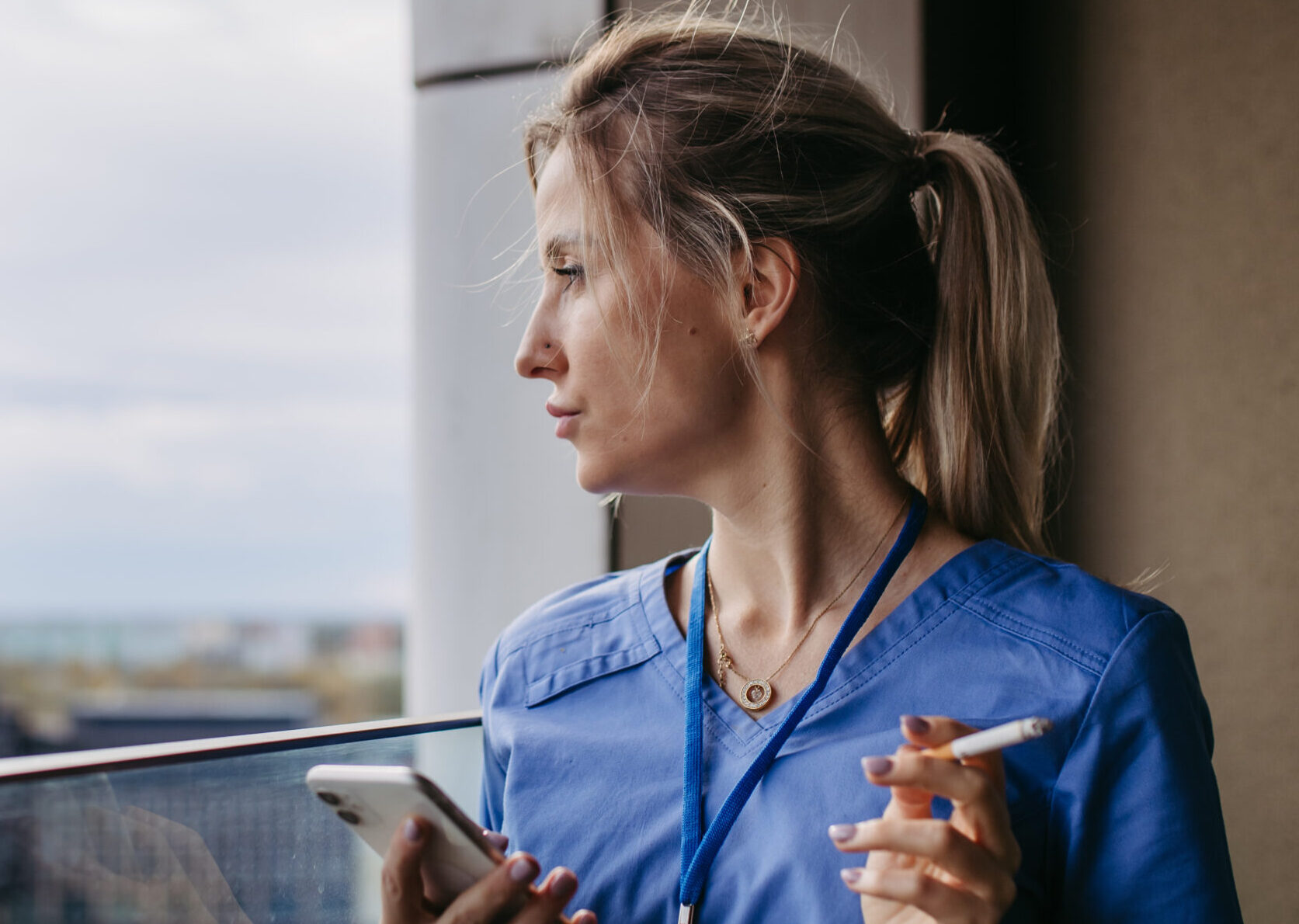 Nurse smoking cigarette at balcony after work. Doctor feeling overwhelmed at work, taking break. Stresfull at hospital, clinic.